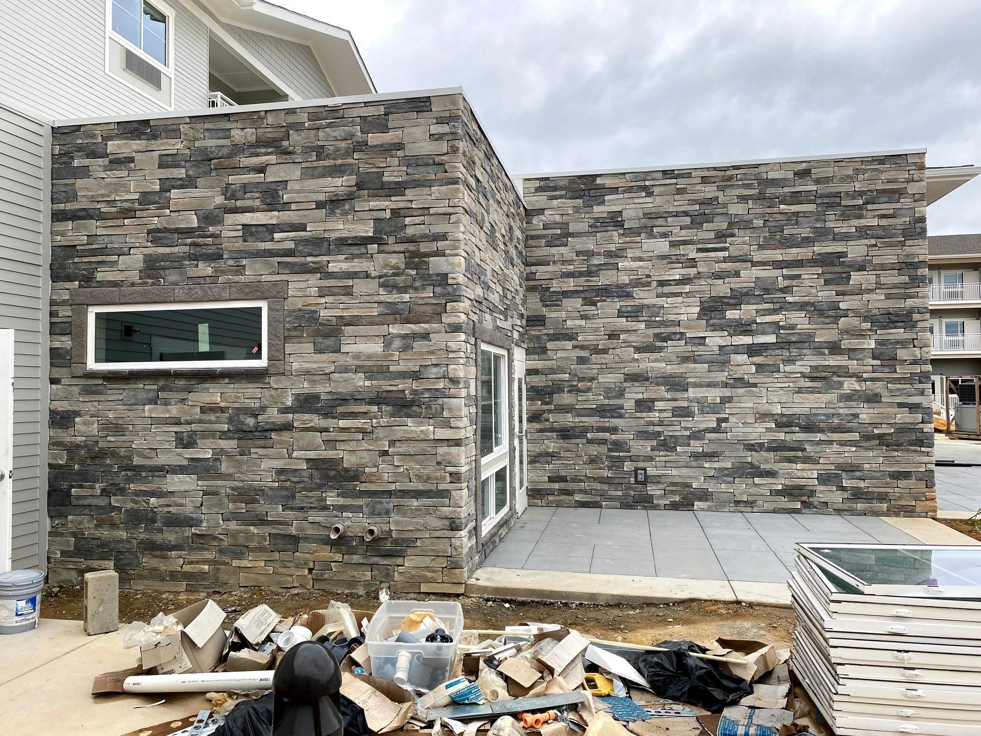 Stone-clad house exterior with construction debris and stacked siding in the yard