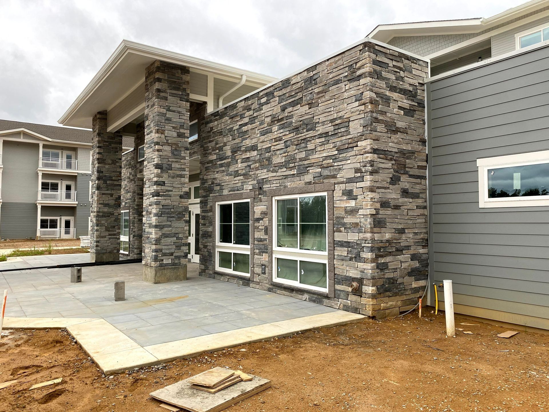 New apartment building entrance with stone facade, gray siding, and concrete patio under construction