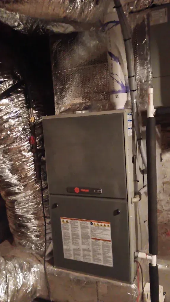 Gray furnace in a utility room surrounded by shiny silver insulated ducts.