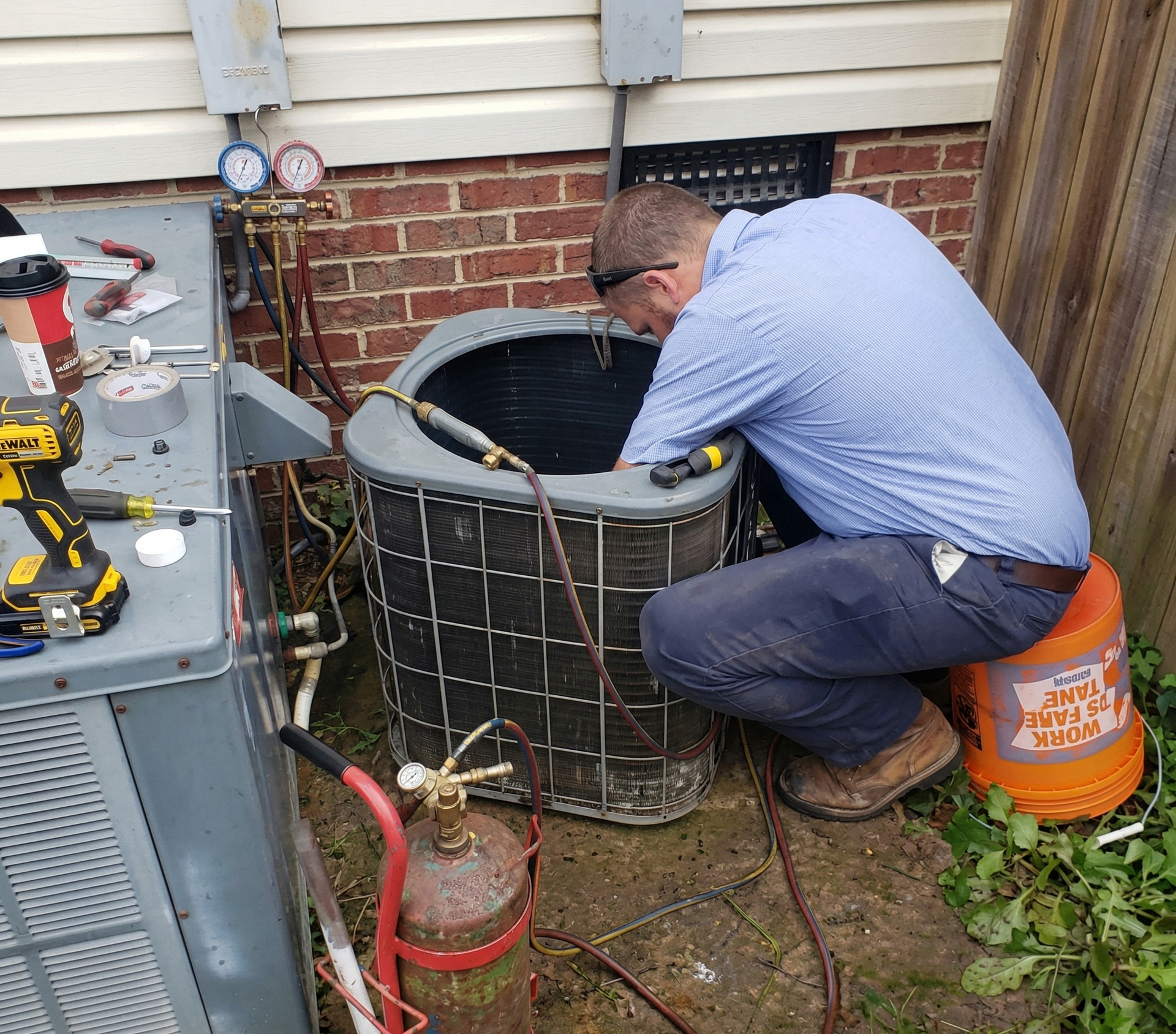 Technician kneels beside an outdoor HVAC unit, checking connections with tools in a backyard.