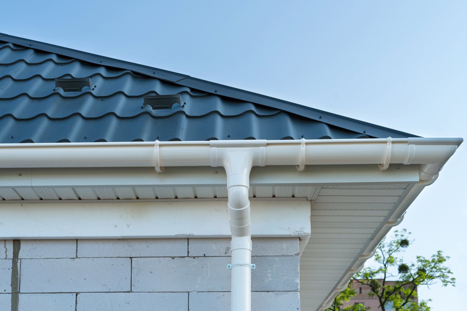 White house gutter and downspout under a blue tiled roof against the sky