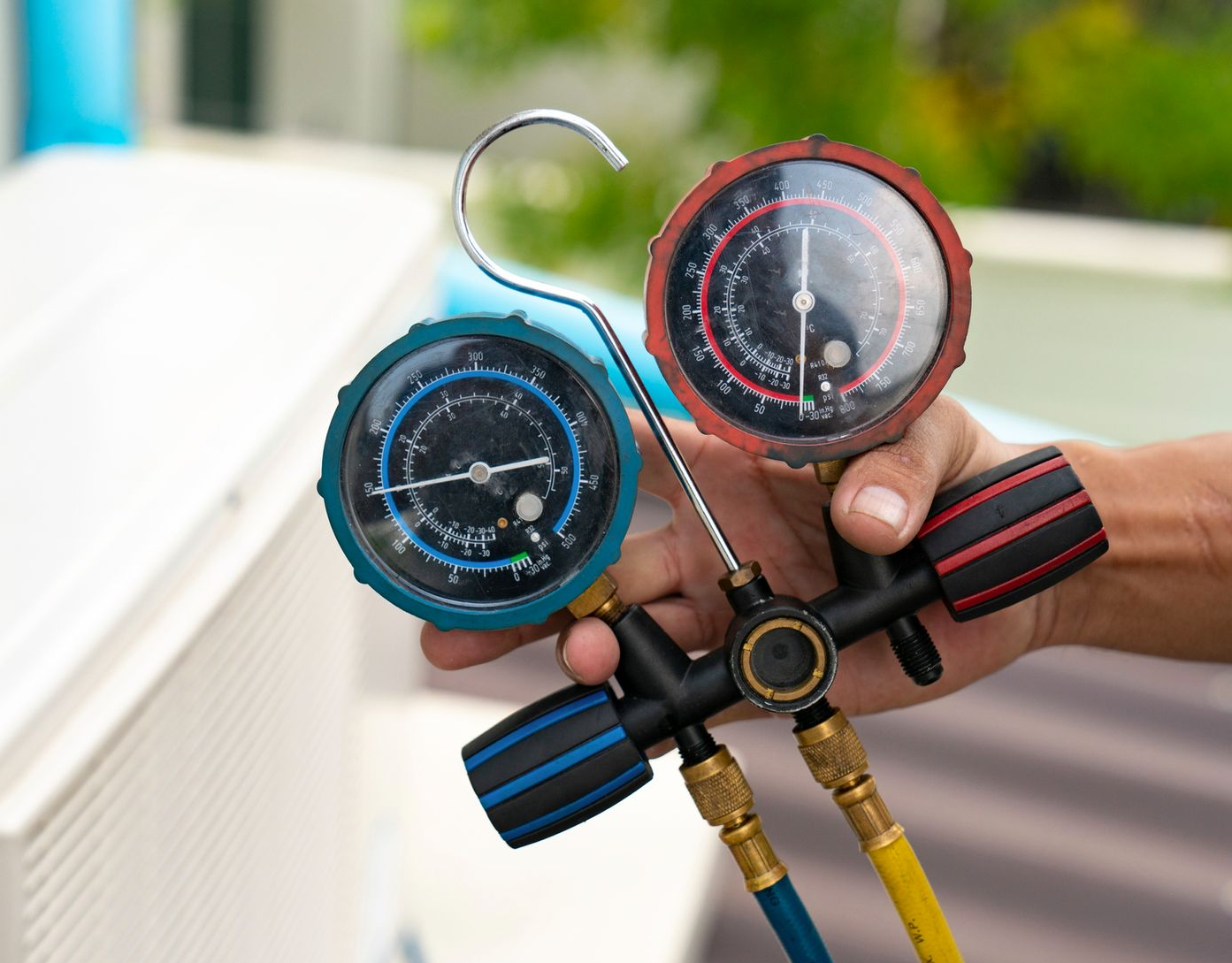 AC unit’s valve is in the hands of a technician, with the AC unit blurred in the back.