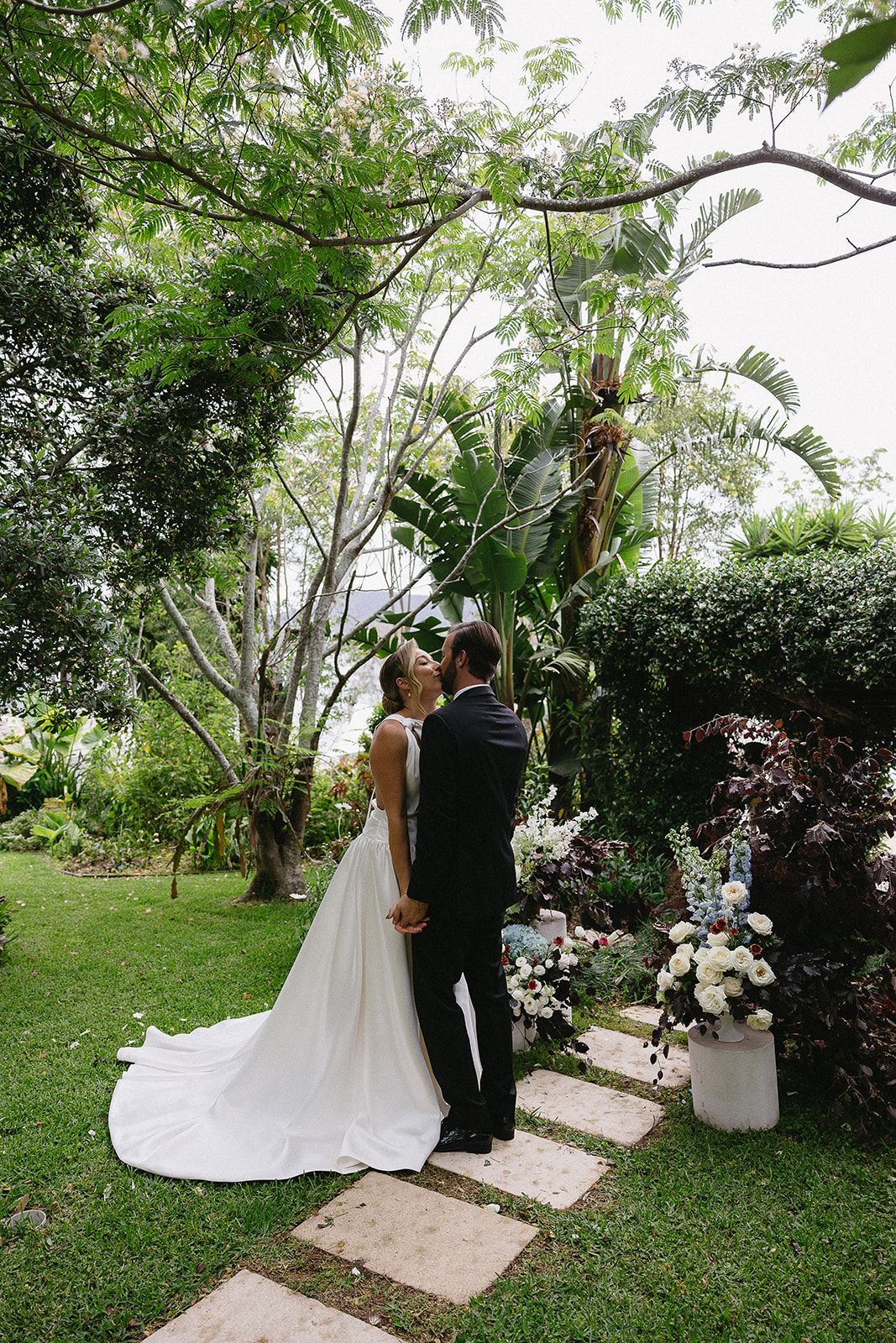 A bride and groom are kissing in a garden.