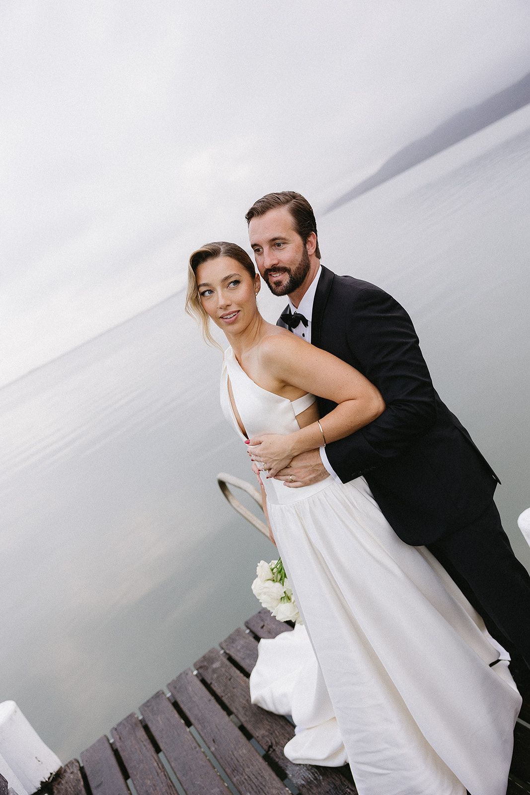 A bride and groom are posing for a picture on a dock.