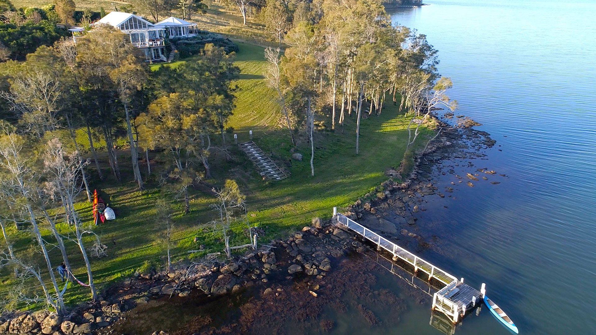 An aerial view of a dock and a house on the shore of a lake.