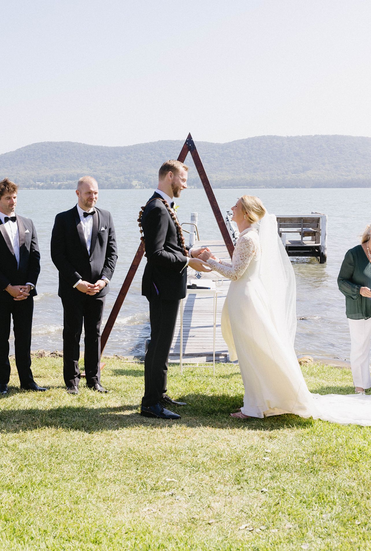 A bride and groom are holding hands during their wedding ceremony in front of a lake.