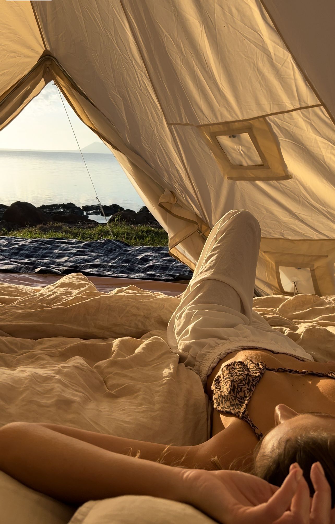 A woman in a bikini is laying on a bed in a tent.