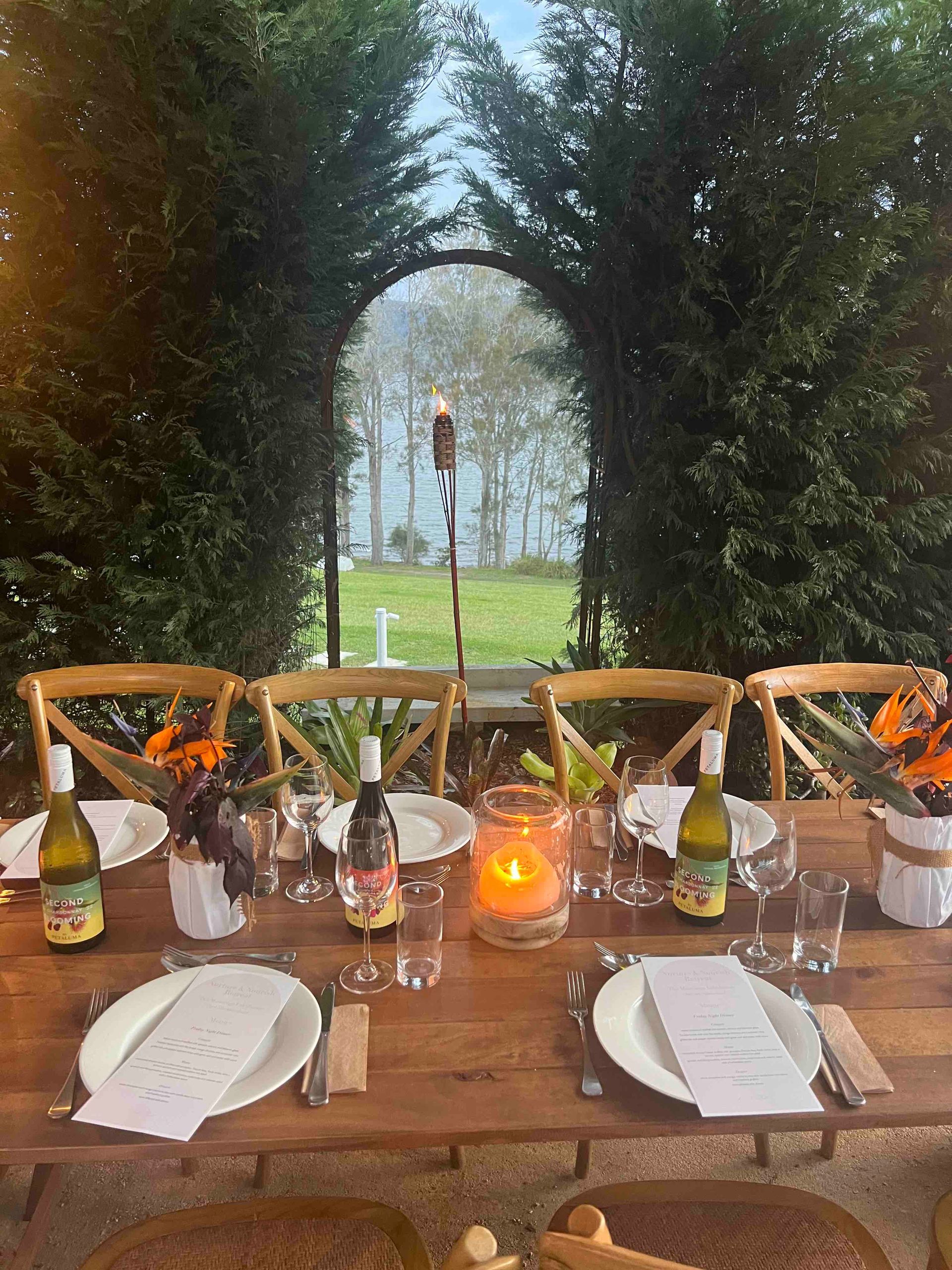 A wooden table with plates , glasses , candles and wine bottles.