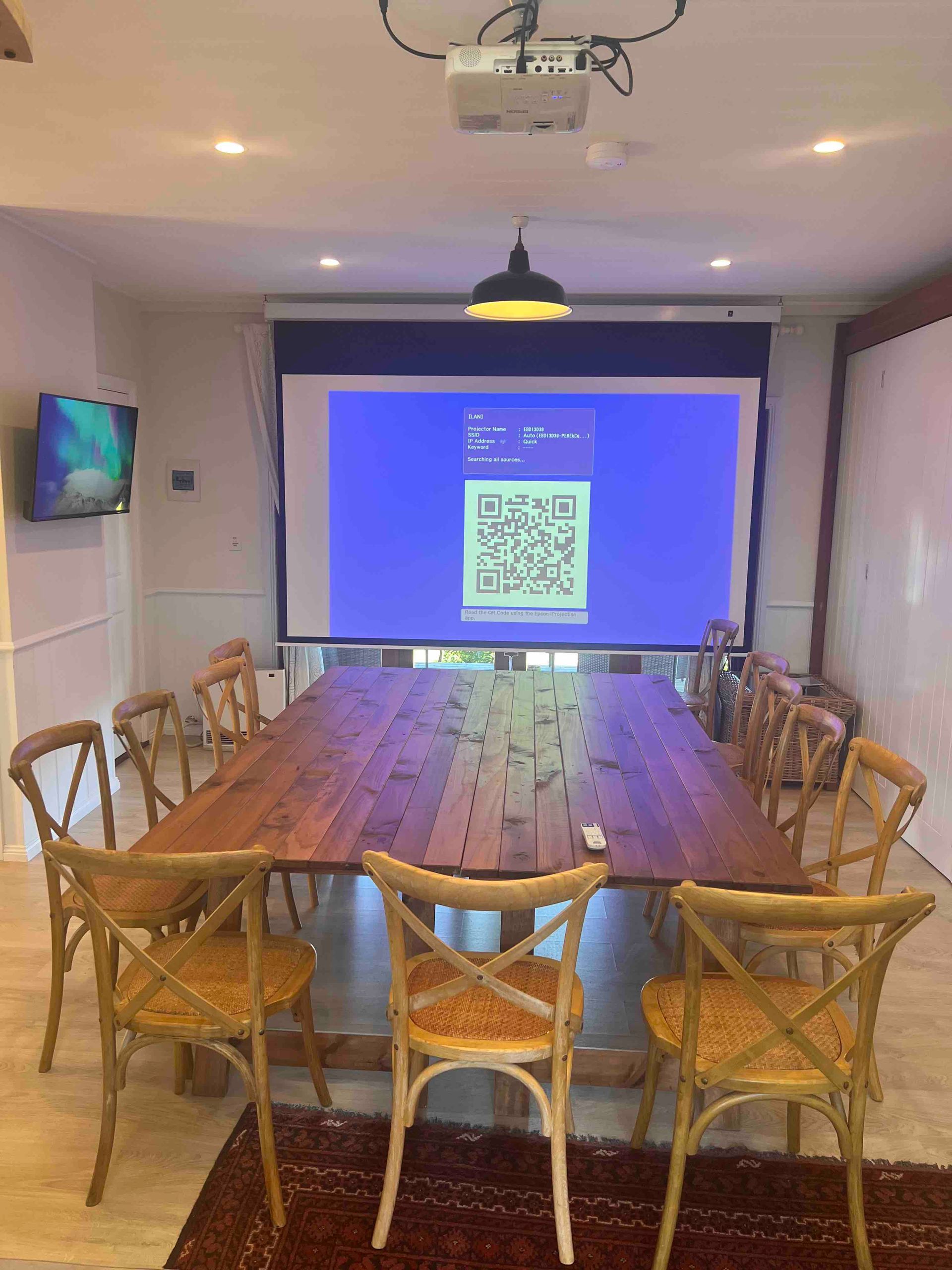 A conference room with a long wooden table and chairs and a projector screen.