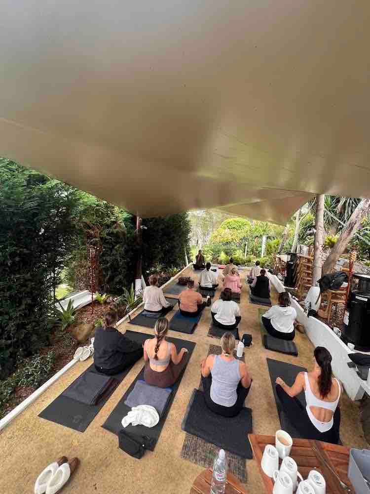 A group of people are sitting on yoga mats under a canopy.