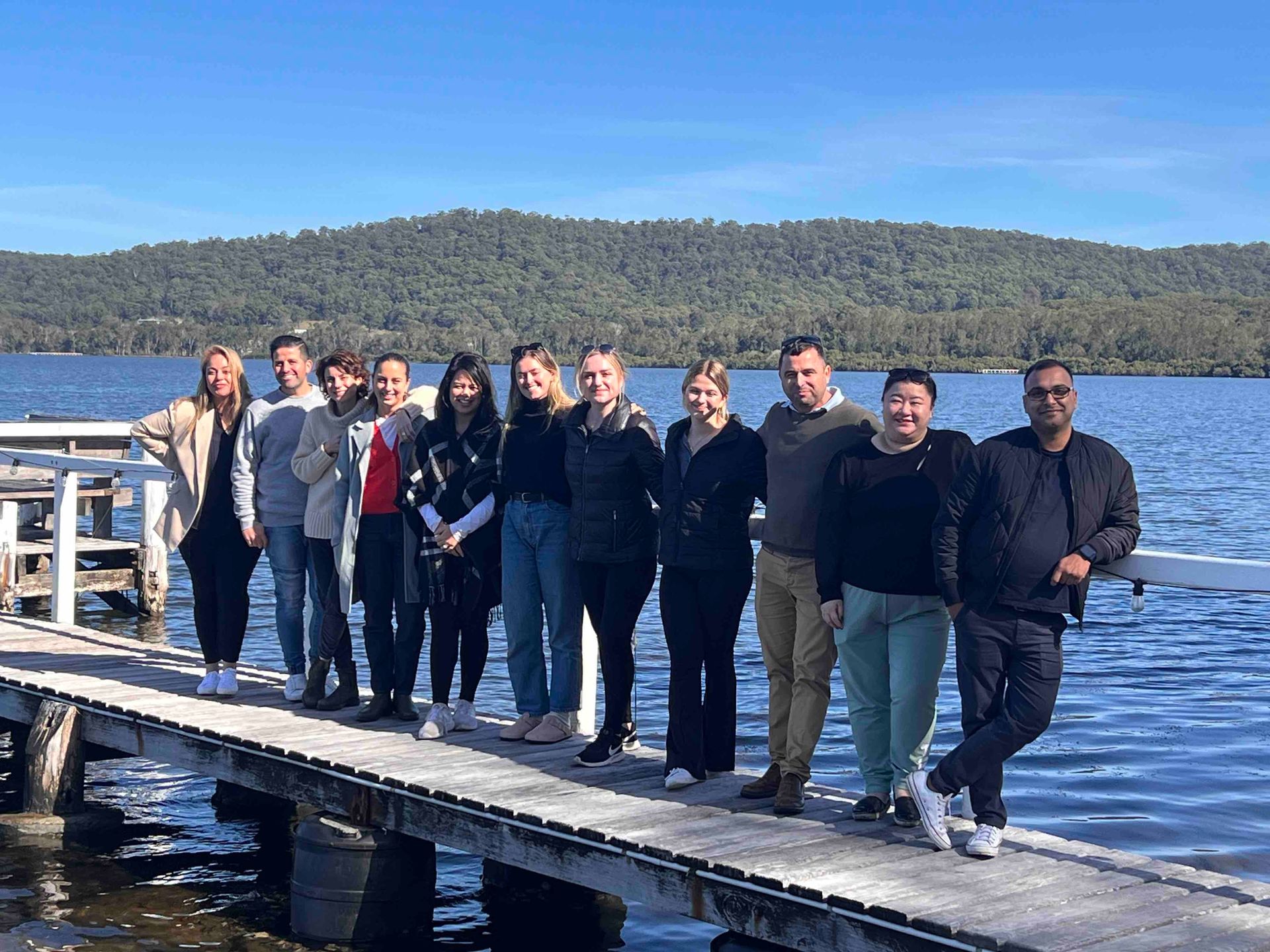 A group of people are standing on a dock next to a lake.