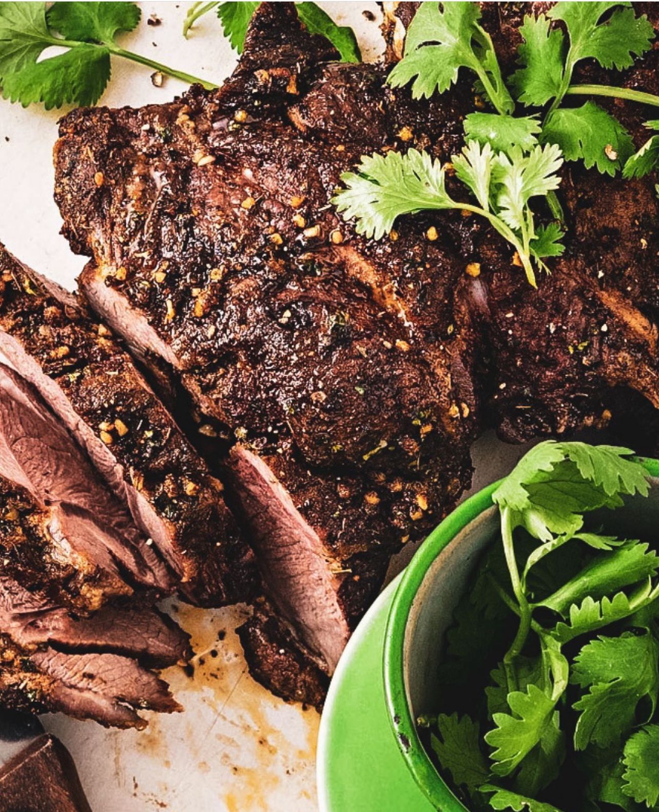 A close up of a piece of meat next to a bowl of cilantro.