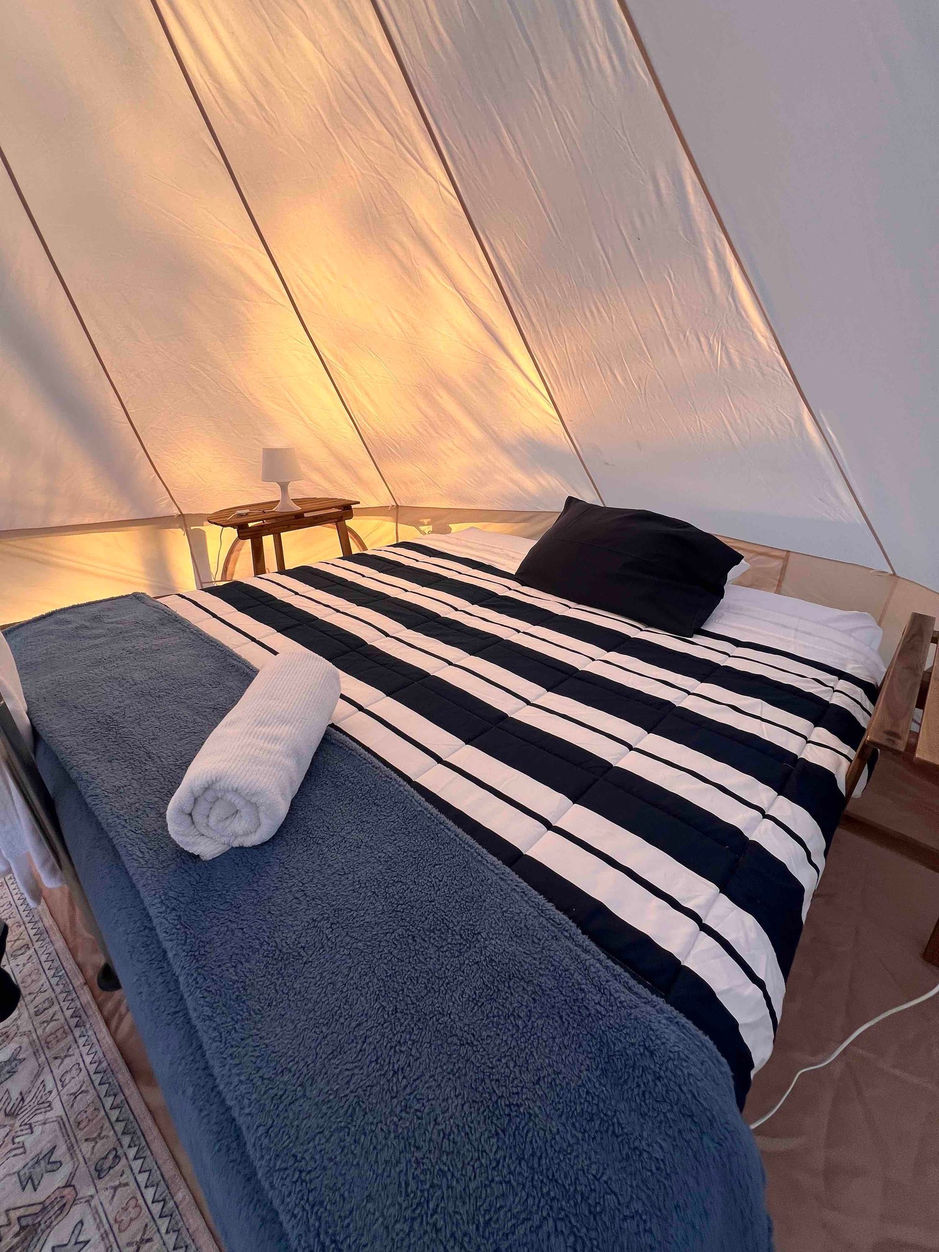 A bed with a striped blanket and pillows in a tent.