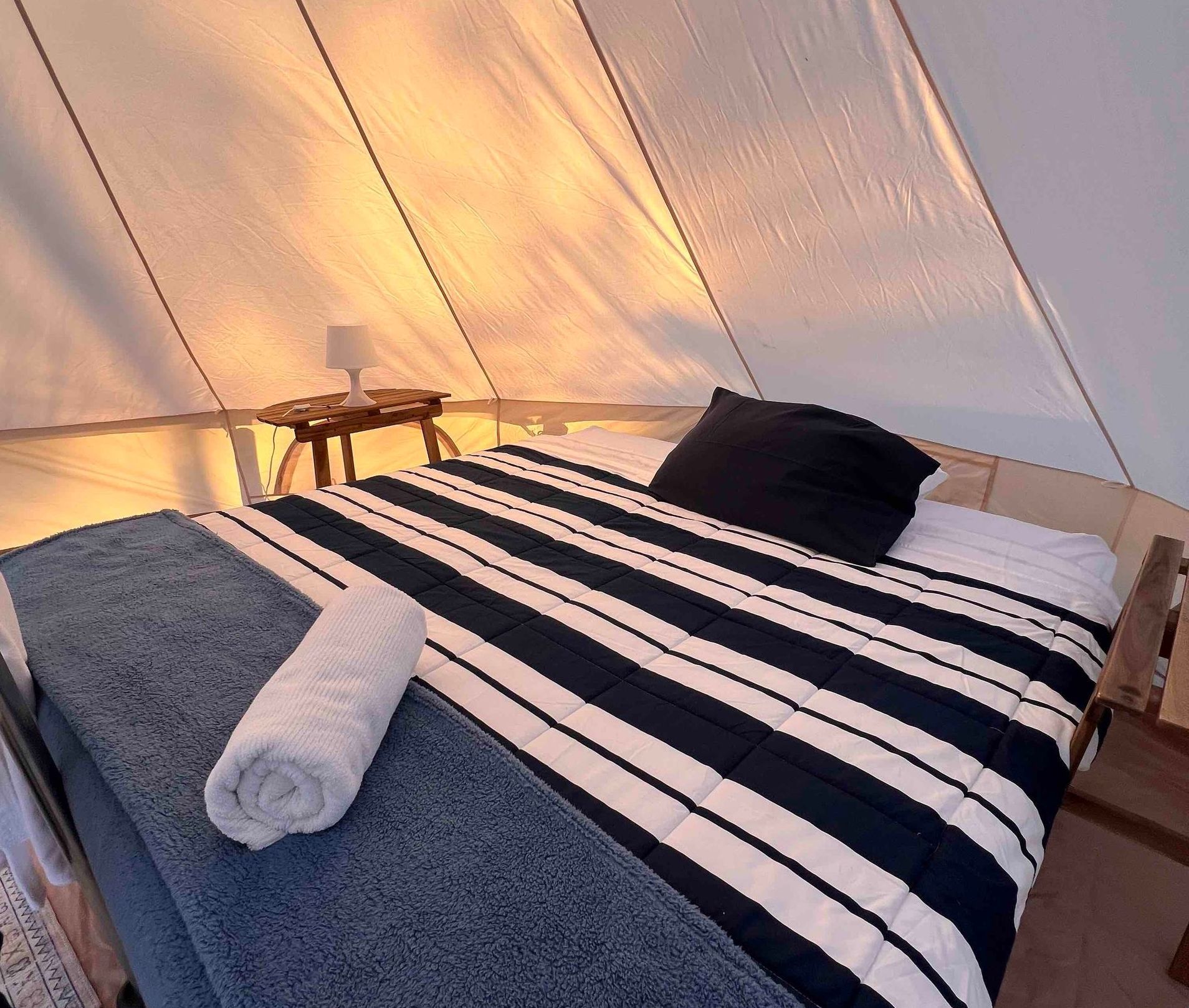 A bed with a striped blanket and two towels on it in a tent.