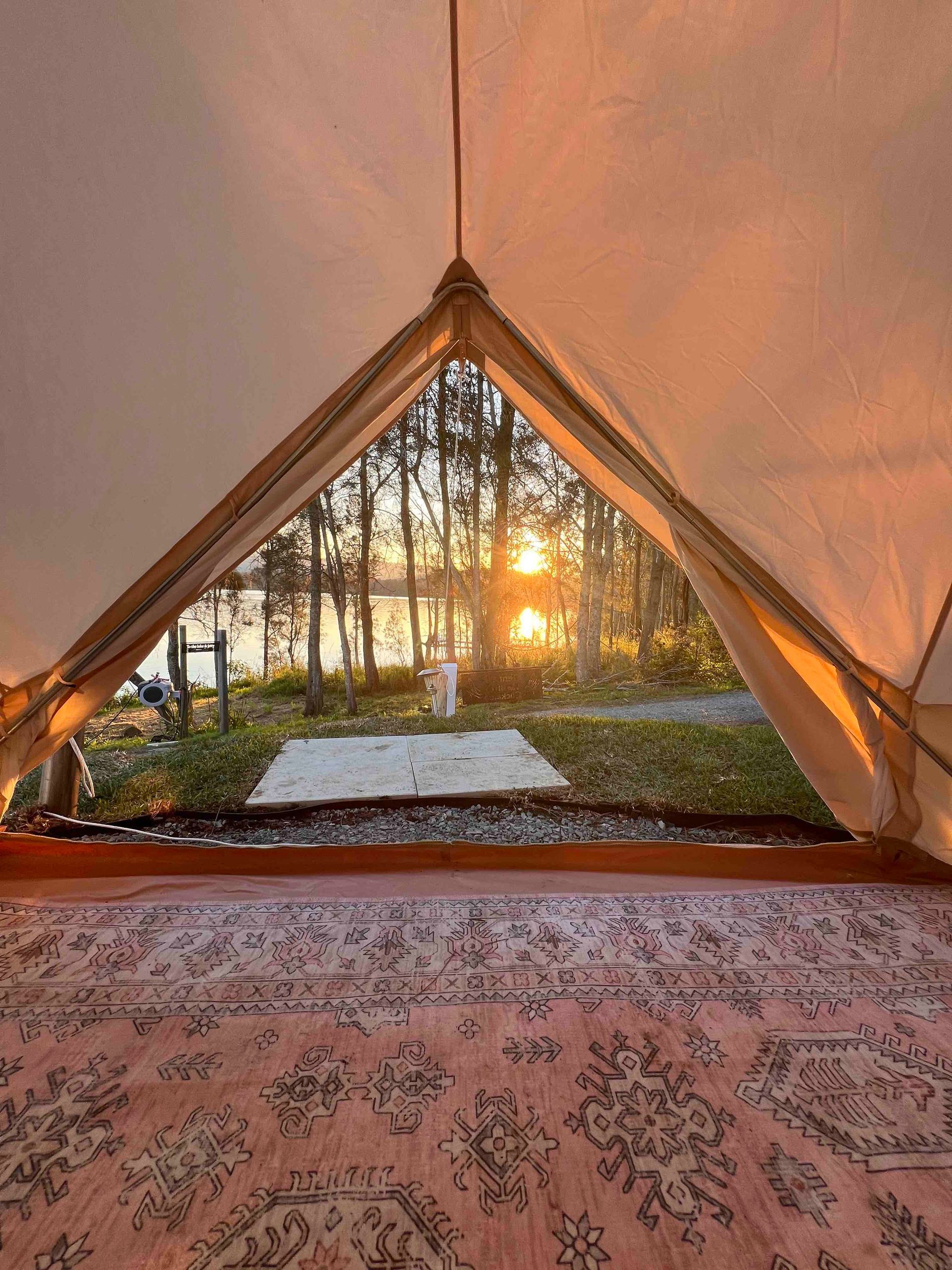A tent with a rug on the floor and a view of the sunset through the window.
