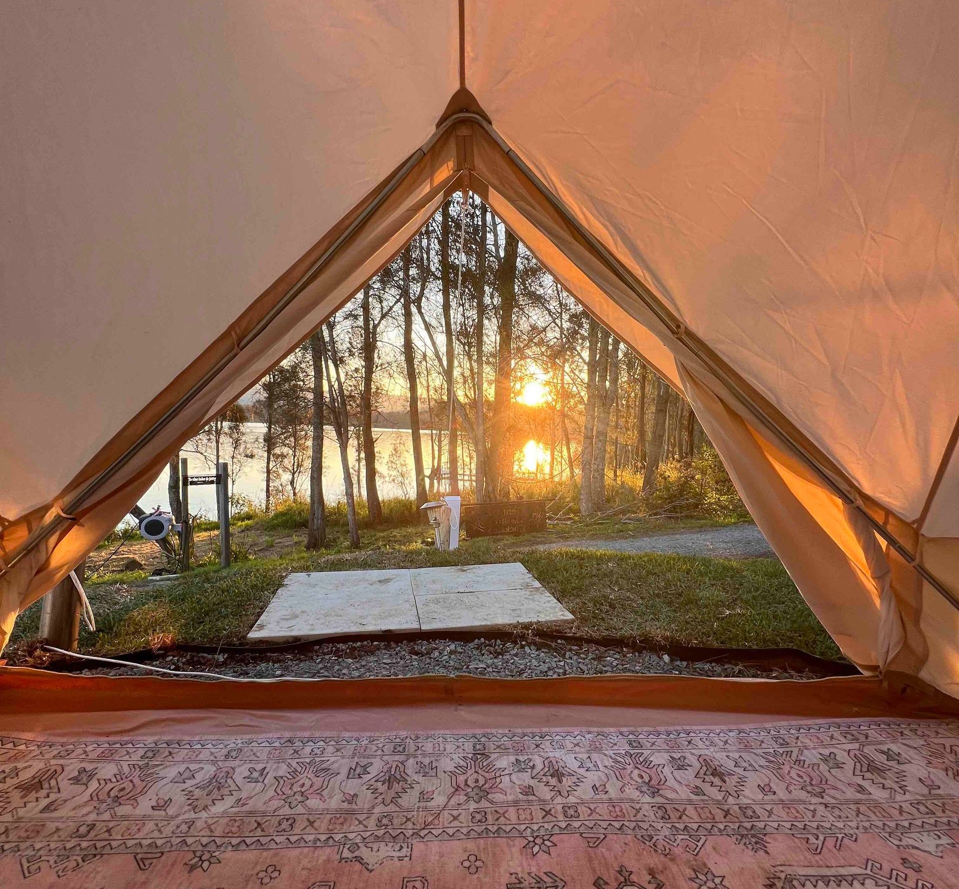 A tent with a view of a lake and trees at sunset.