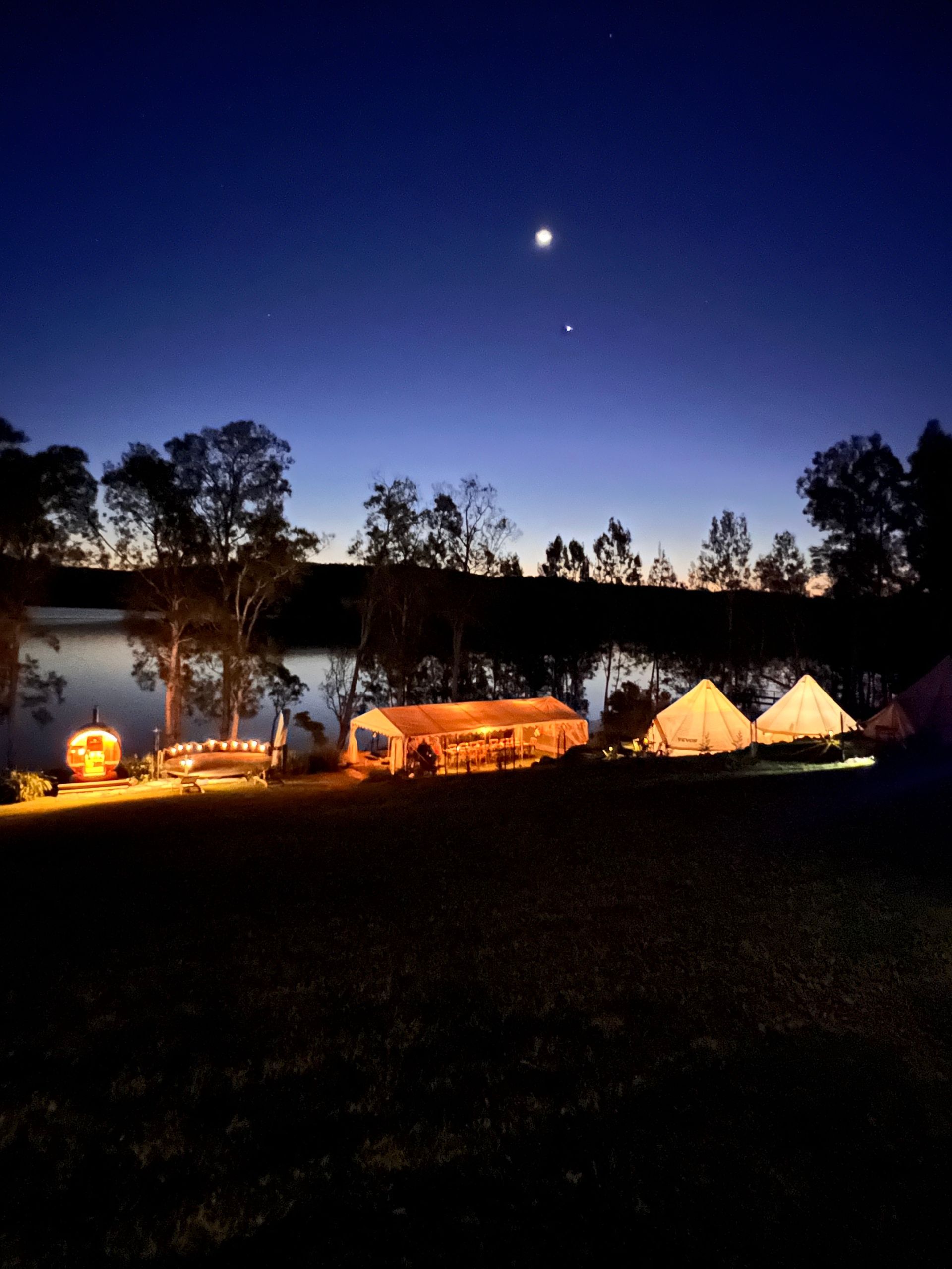 A group of tents are lit up at night near a body of water