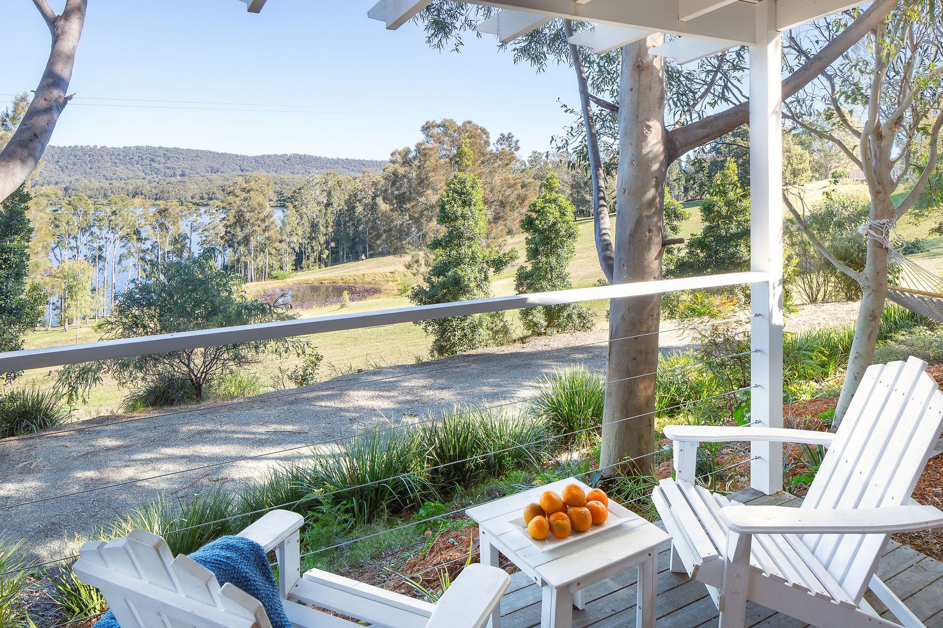 Two white chairs are sitting on a deck overlooking a lake.