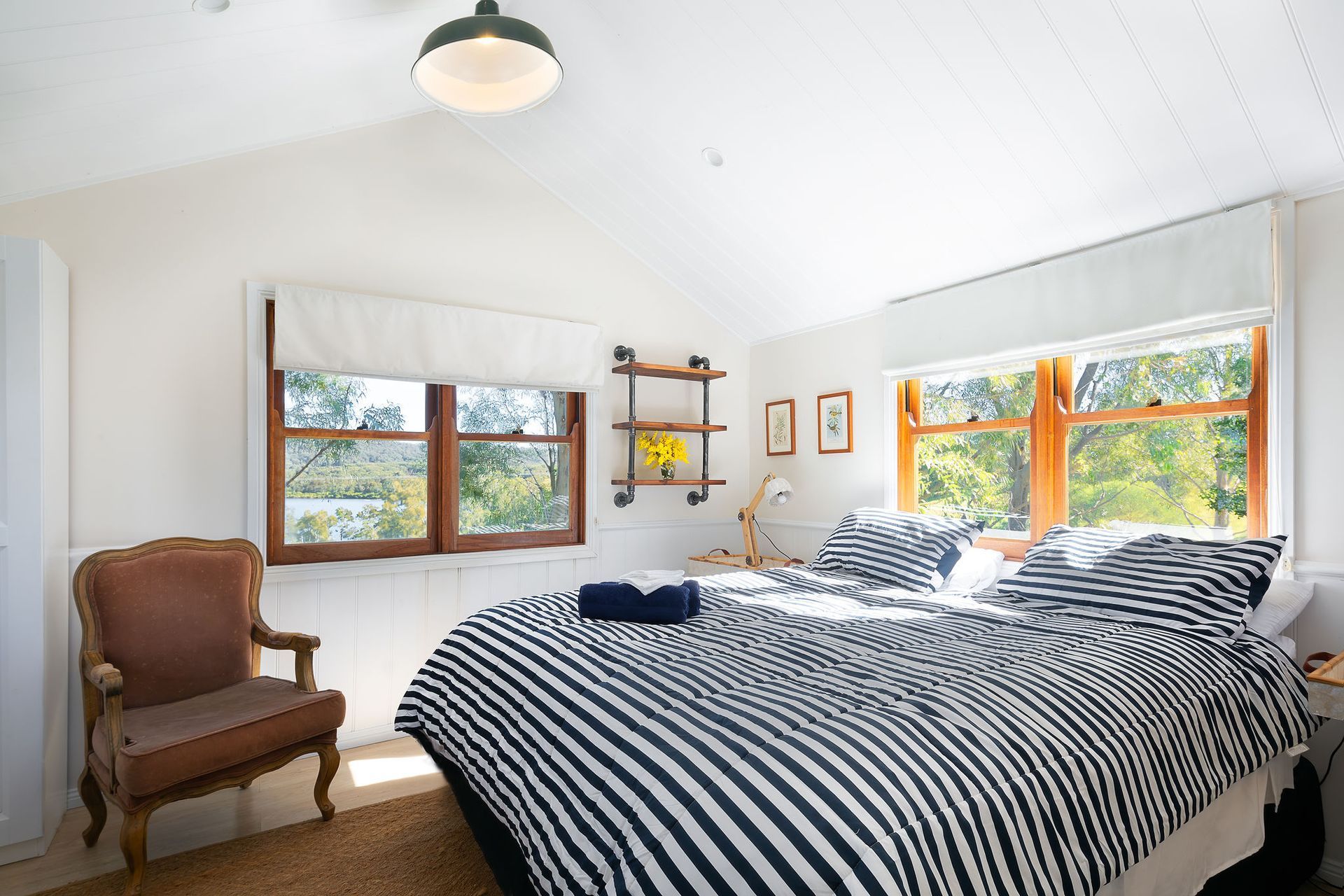 A bedroom with a bed , chair , and two windows.