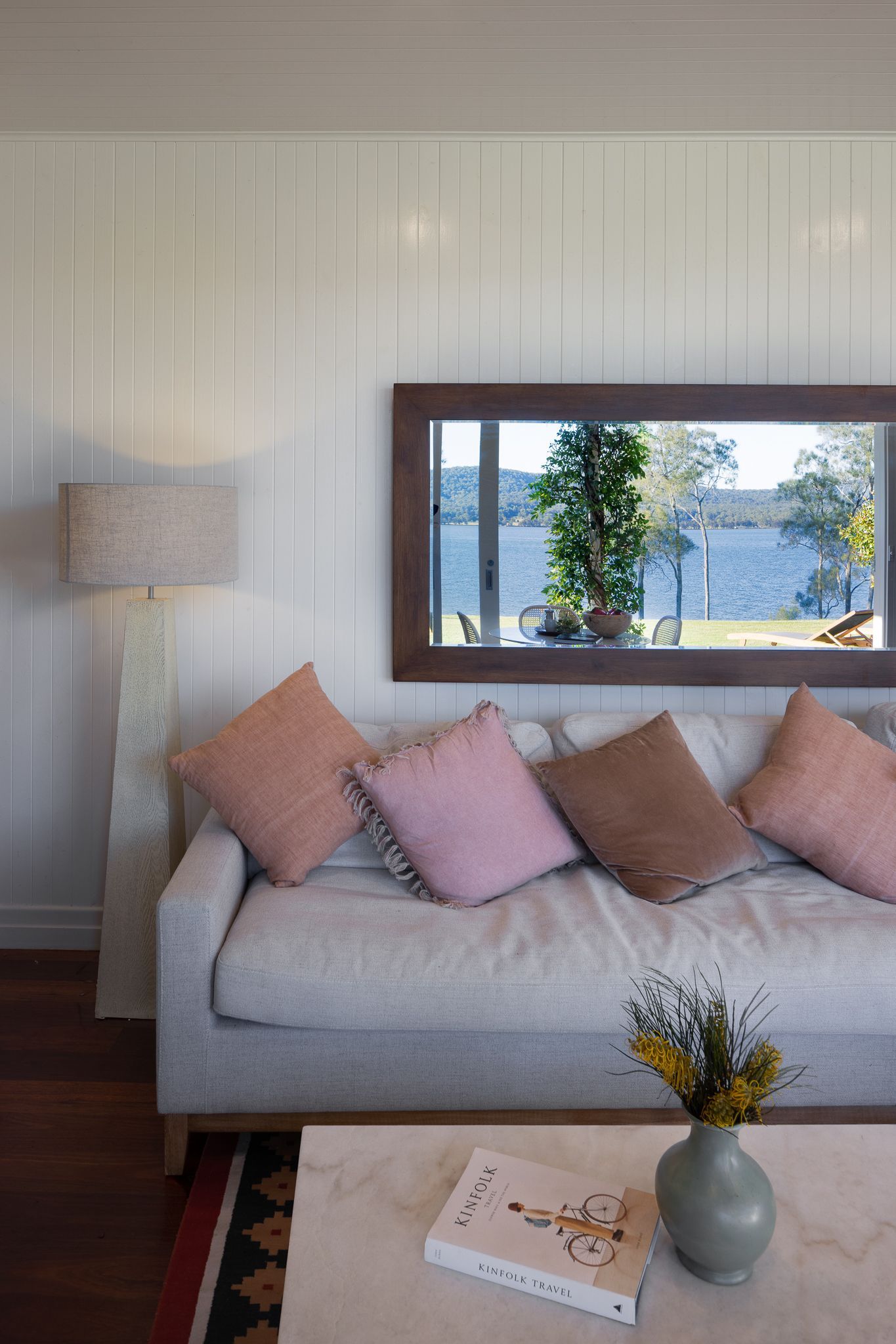 A living room with a couch , table , lamp and mirror.