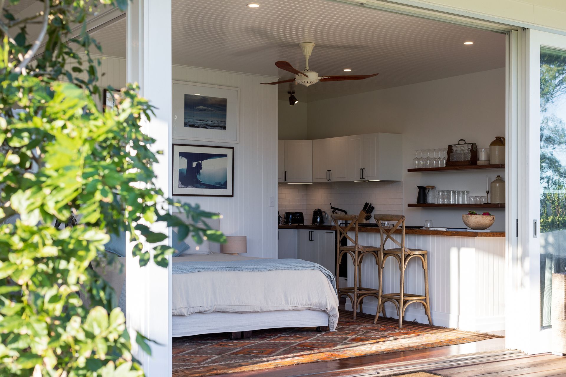 A bedroom with a bed and a kitchen with a ceiling fan.