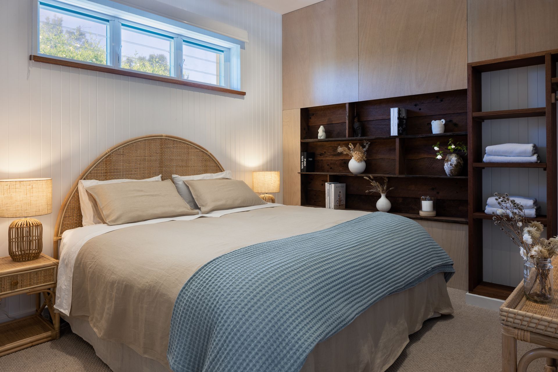 A bedroom with a bed , lamps , shelves and a window.