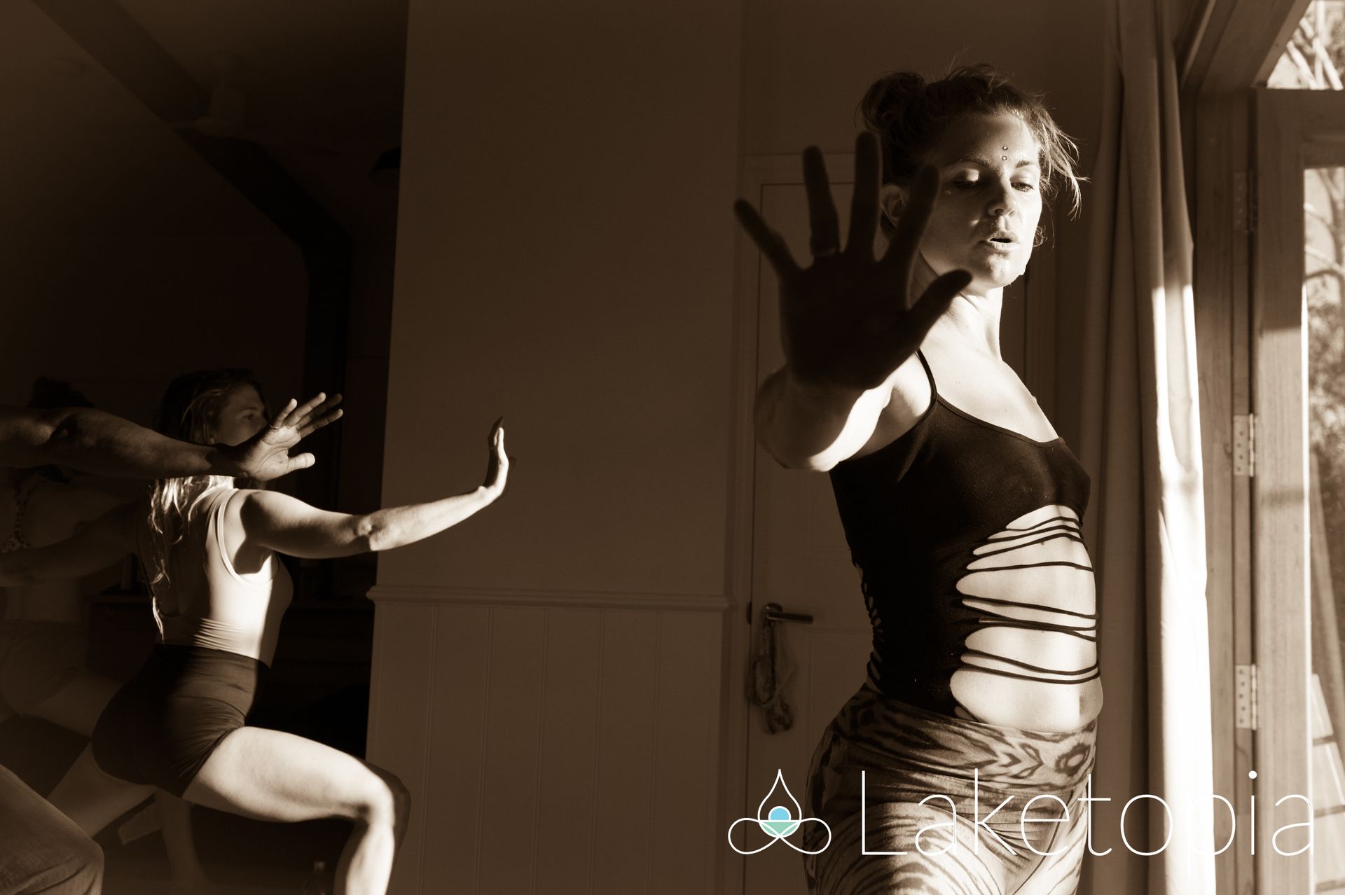 A woman in a black tank top is standing in front of a window.
