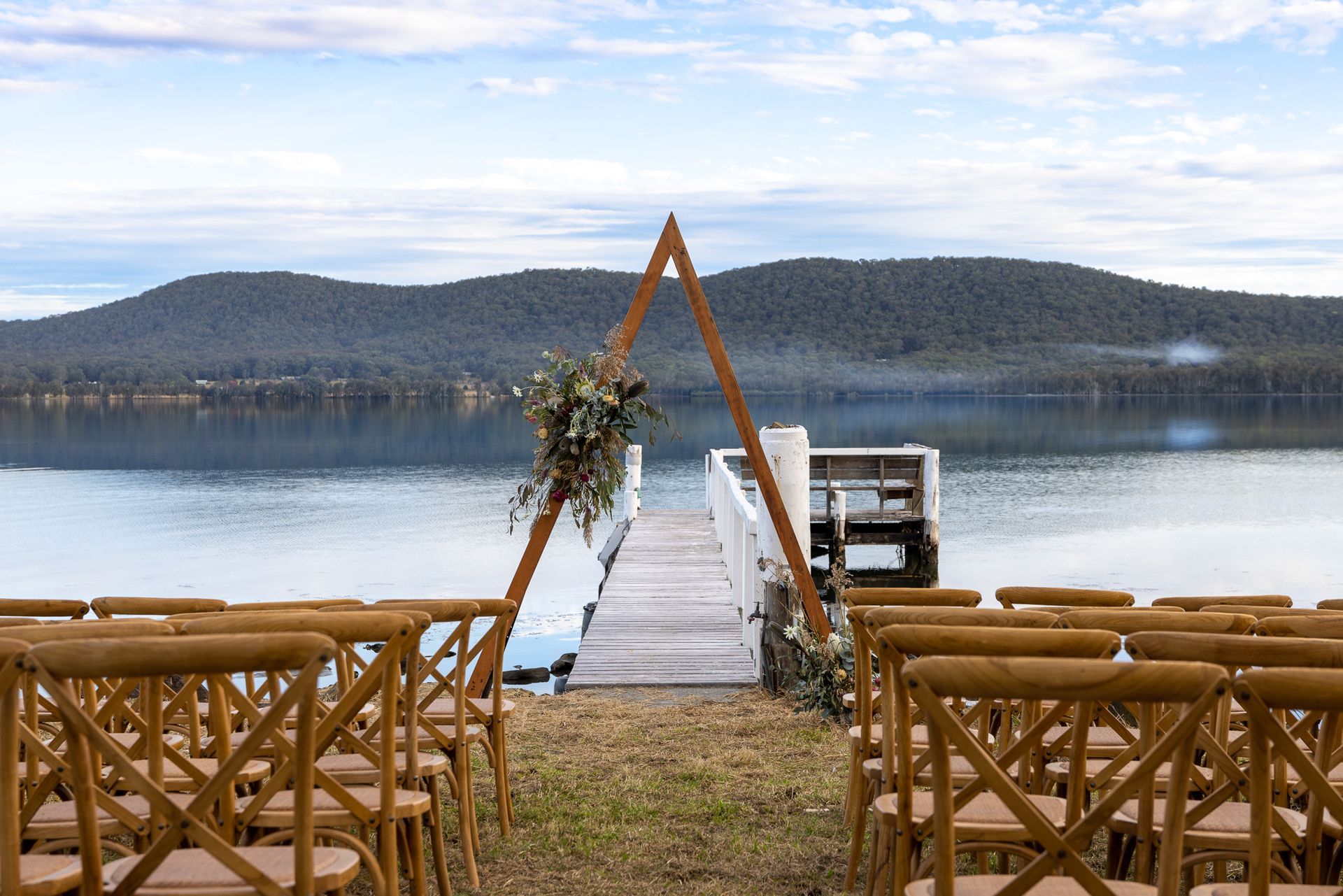 A wedding ceremony is taking place on a dock overlooking a lake.