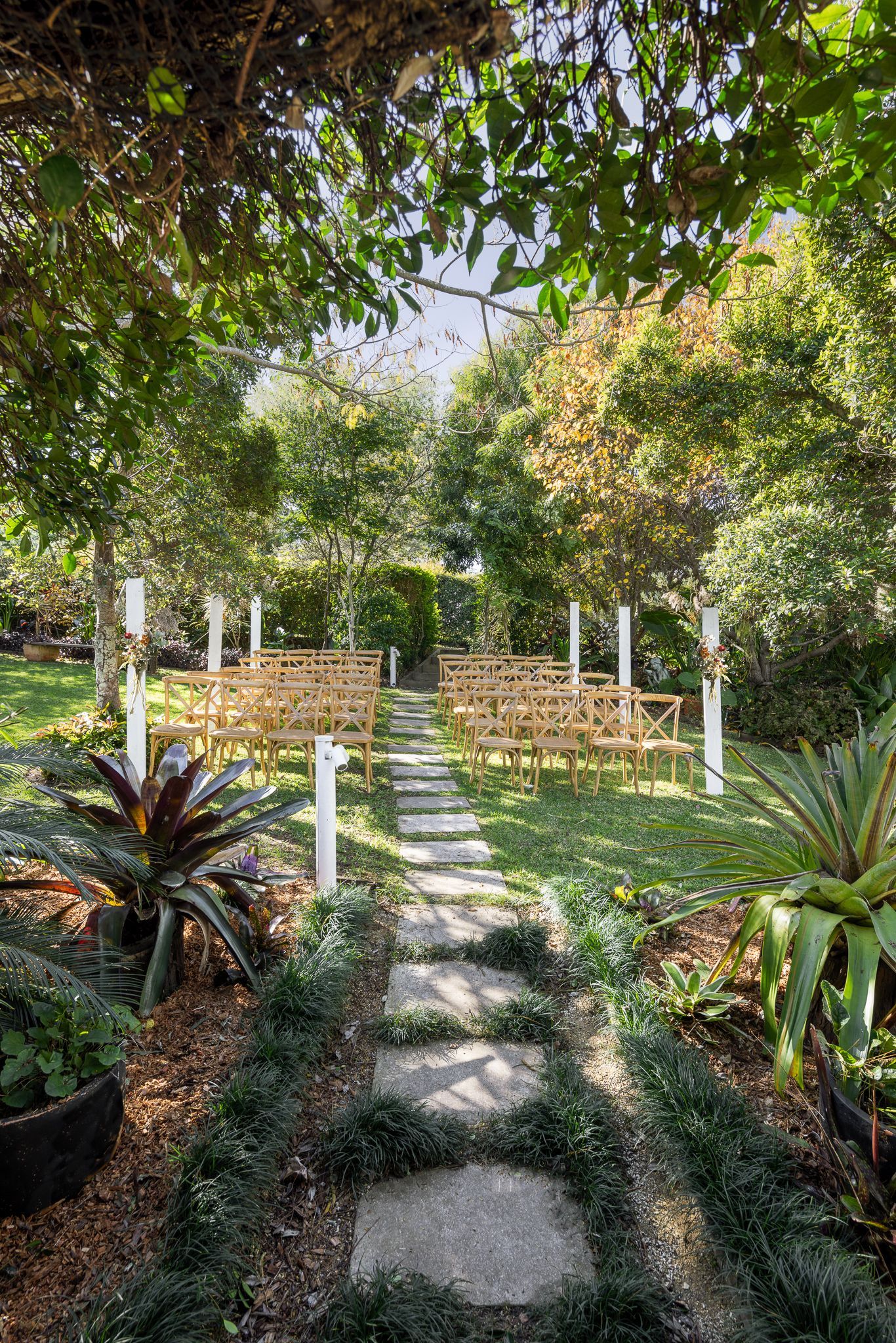 A stone path leading to a wedding ceremony in a garden surrounded by trees.