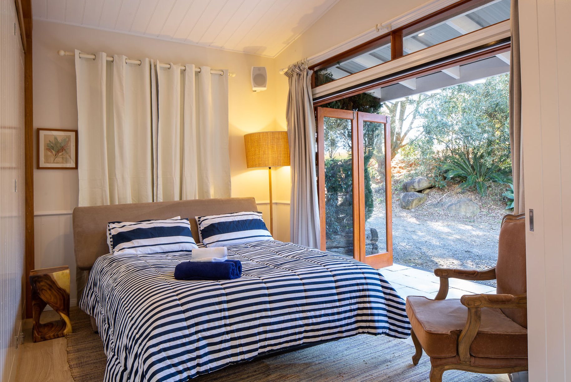 A bedroom with a bed , chair , lamp and sliding glass doors leading to a patio.