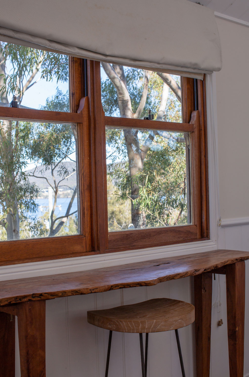 A wooden table with a stool in front of a window with a view of trees.