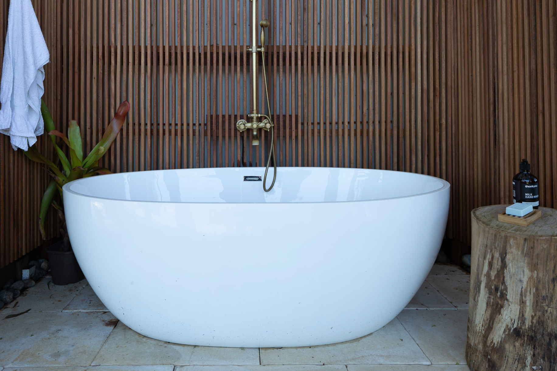 A white bathtub is sitting next to a tree stump in a bathroom.
