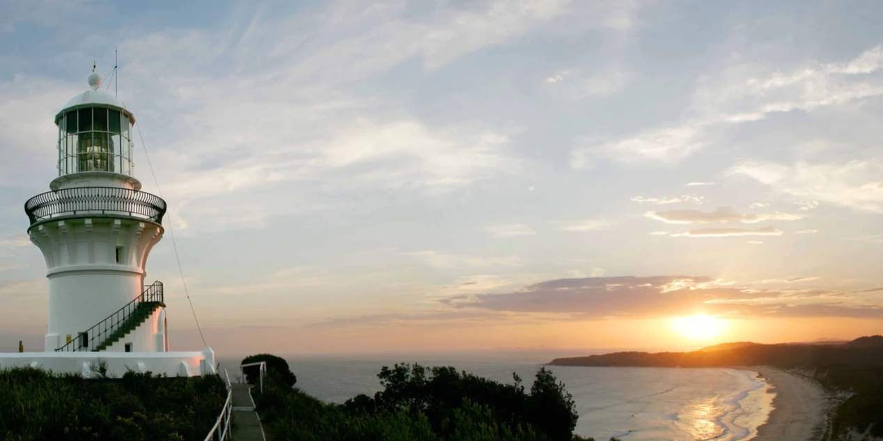 A lighthouse on top of a hill overlooking the ocean at sunset.