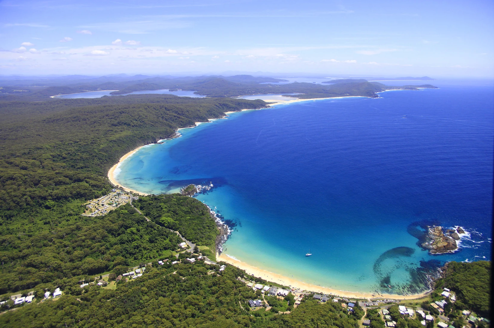 An aerial view of a beach surrounded by trees and a body of water.