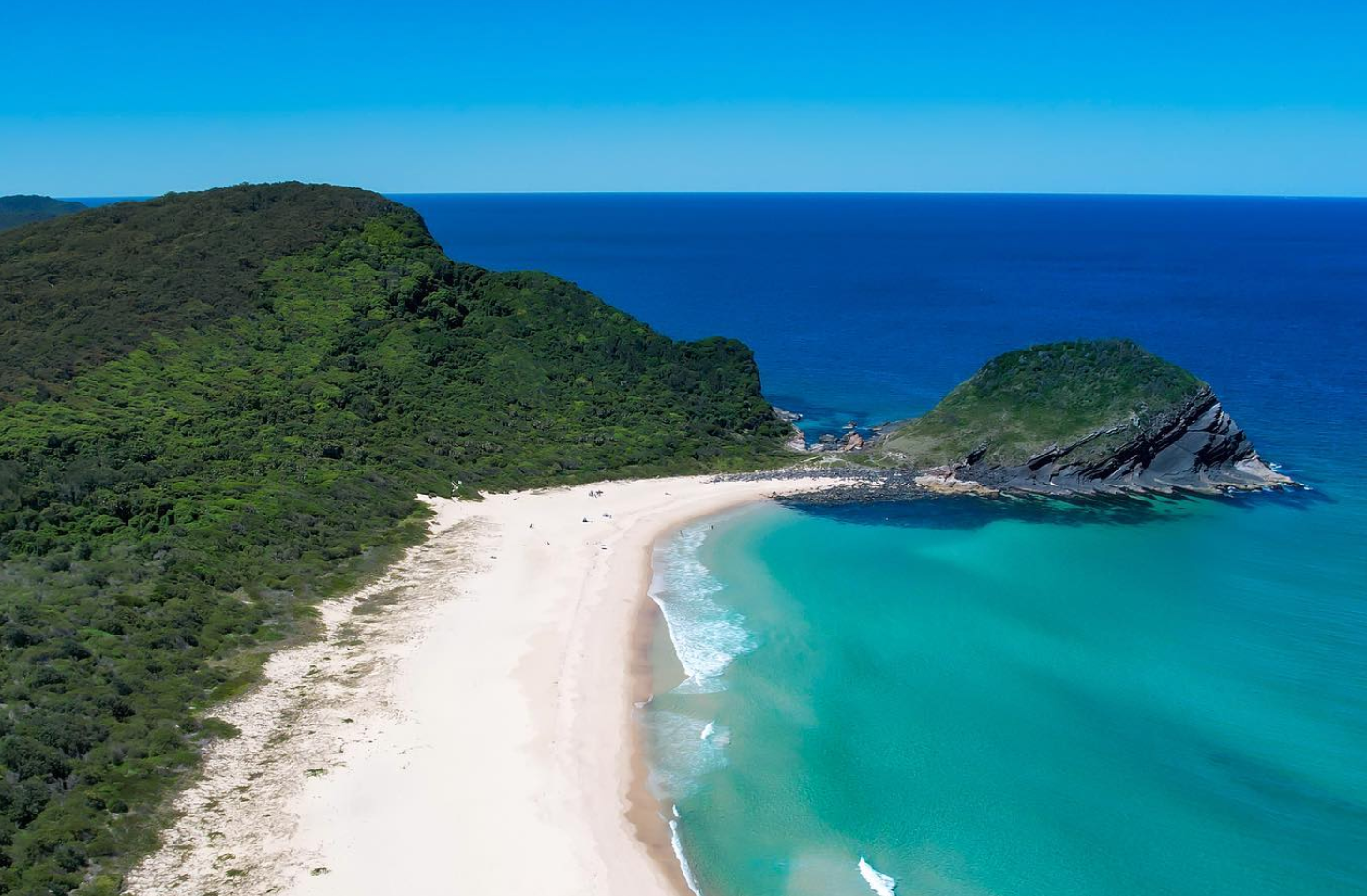An aerial view of a beach with a small island in the middle of the ocean.