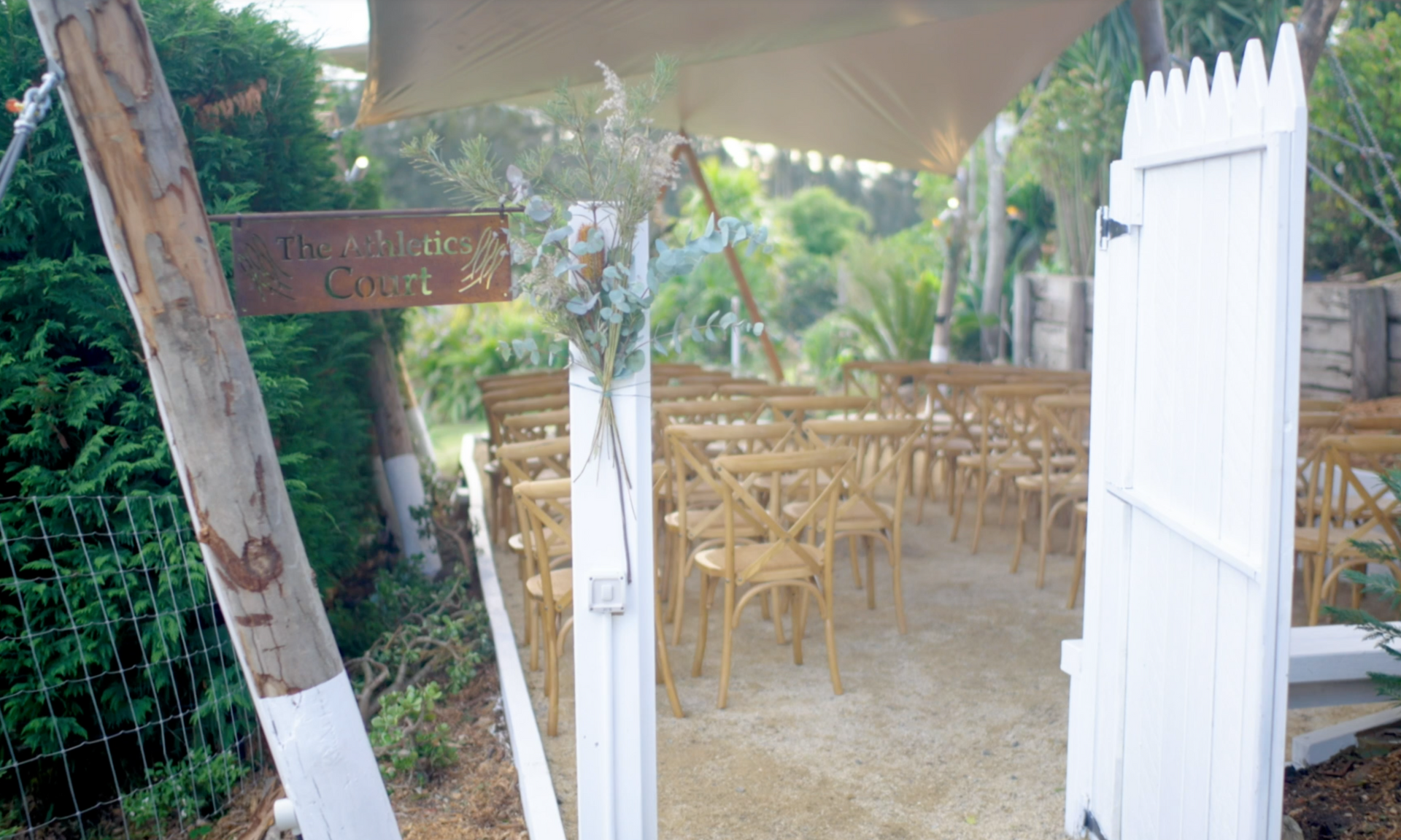 A wedding ceremony is taking place under a canopy in the woods.