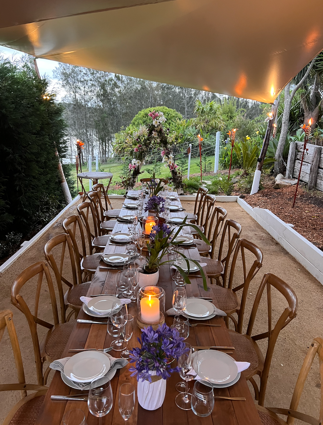 A long wooden table with plates , glasses , candles and flowers on it.