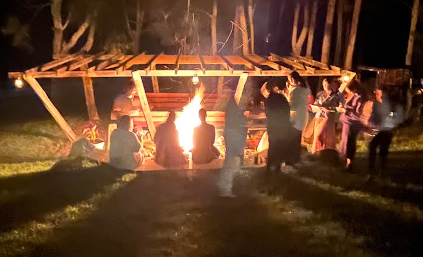 A group of people are sitting around a campfire at night.