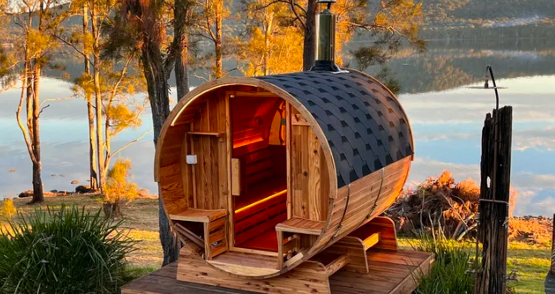 A wooden barrel sauna is sitting next to a lake.