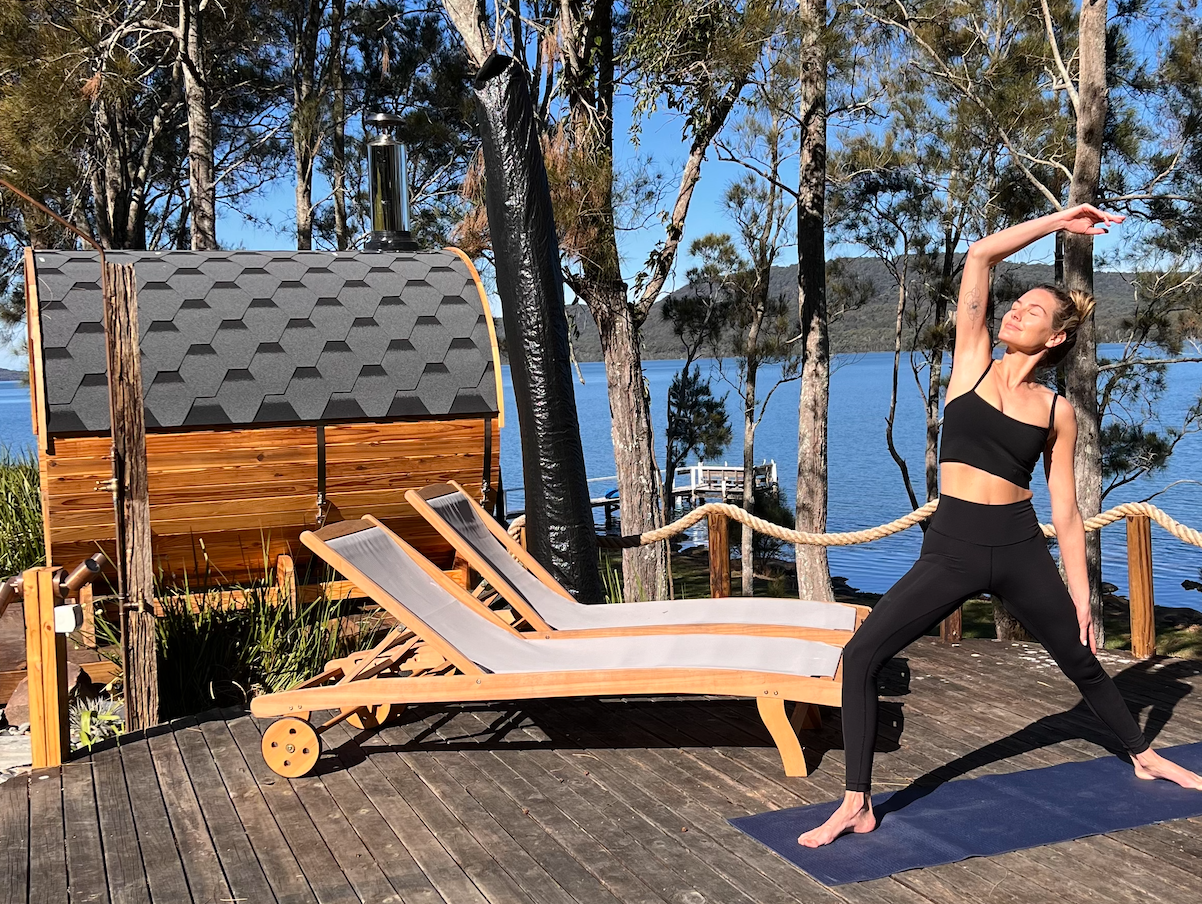 A woman is doing yoga on a deck next to a body of water.