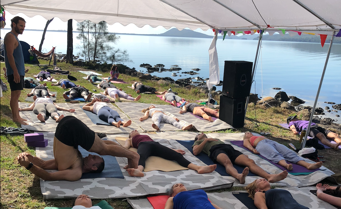 A group of people are laying on yoga mats under a tent.