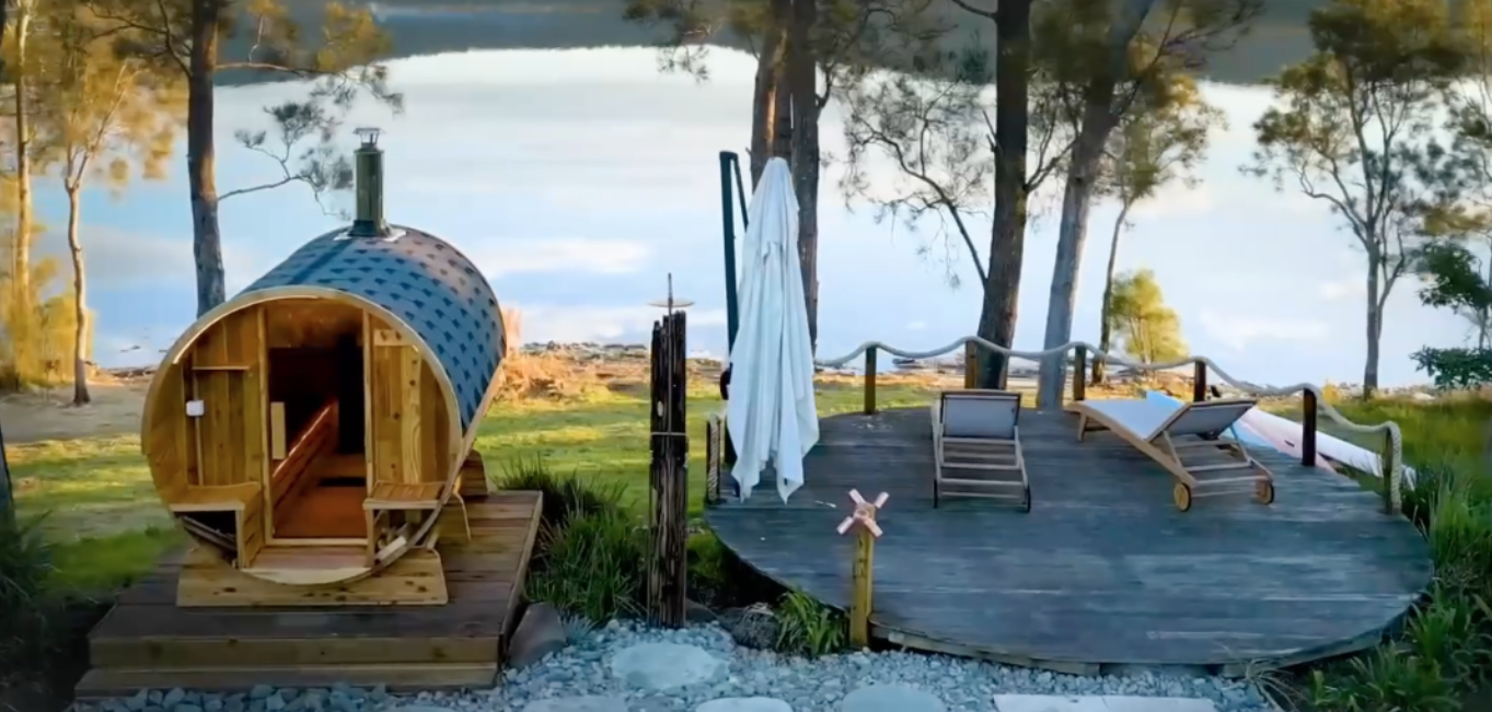 A wooden sauna is sitting on top of a wooden deck next to a lake.