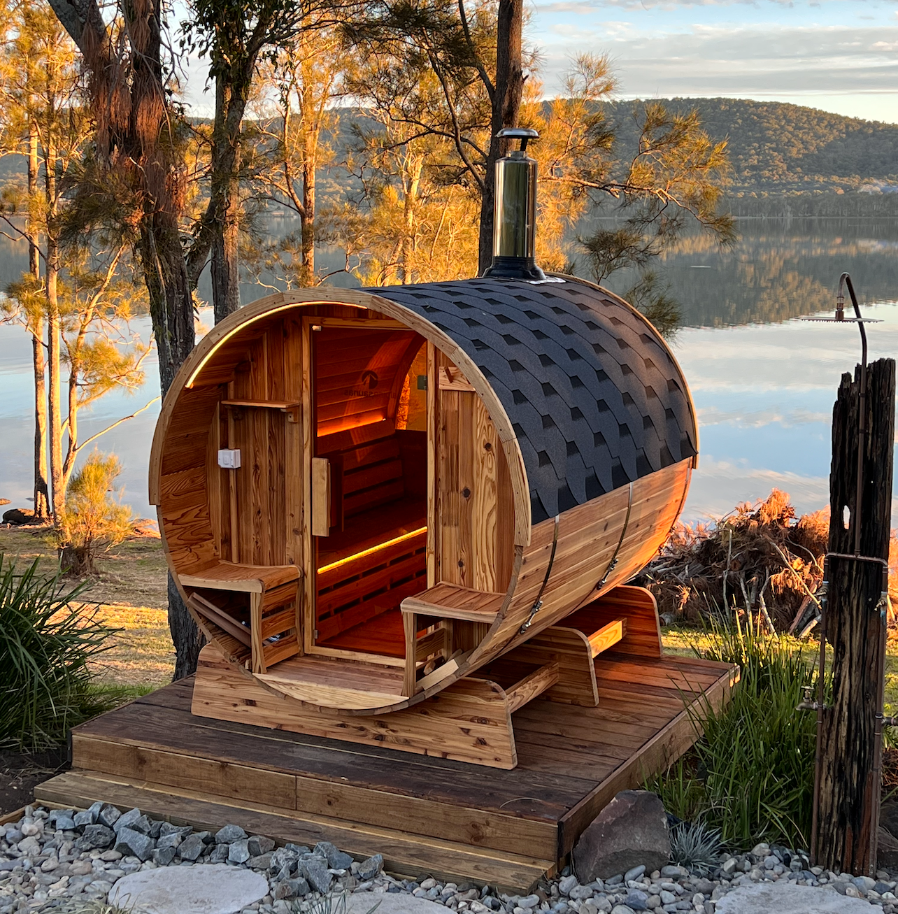 A wooden barrel sauna is sitting next to a lake.