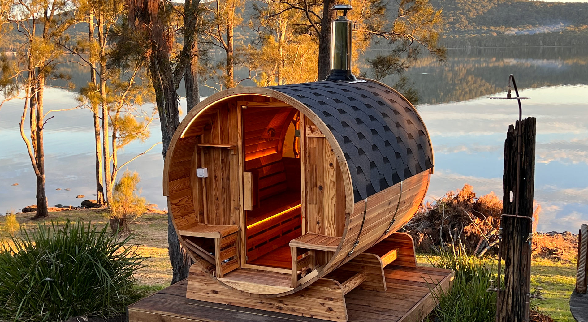 A wooden barrel sauna is sitting next to a lake.