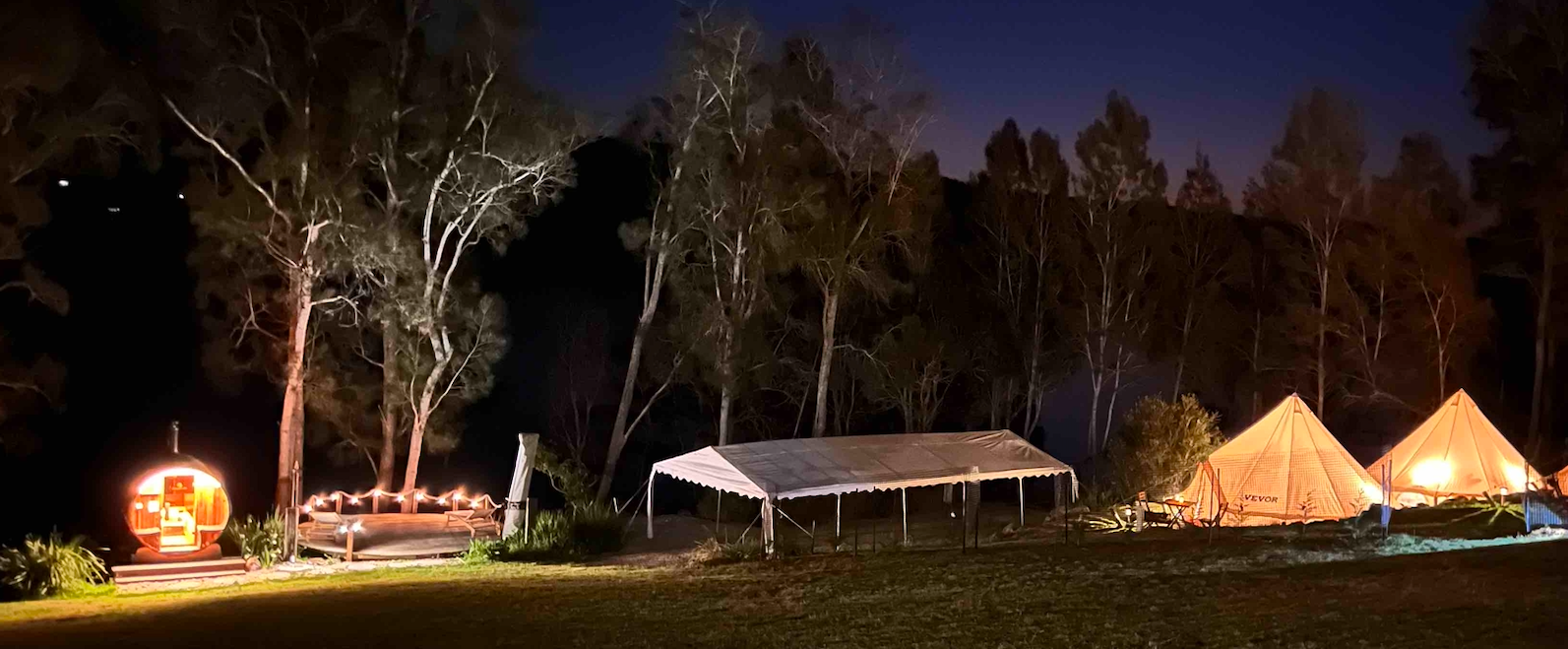 A group of tents are lit up in a field at night.