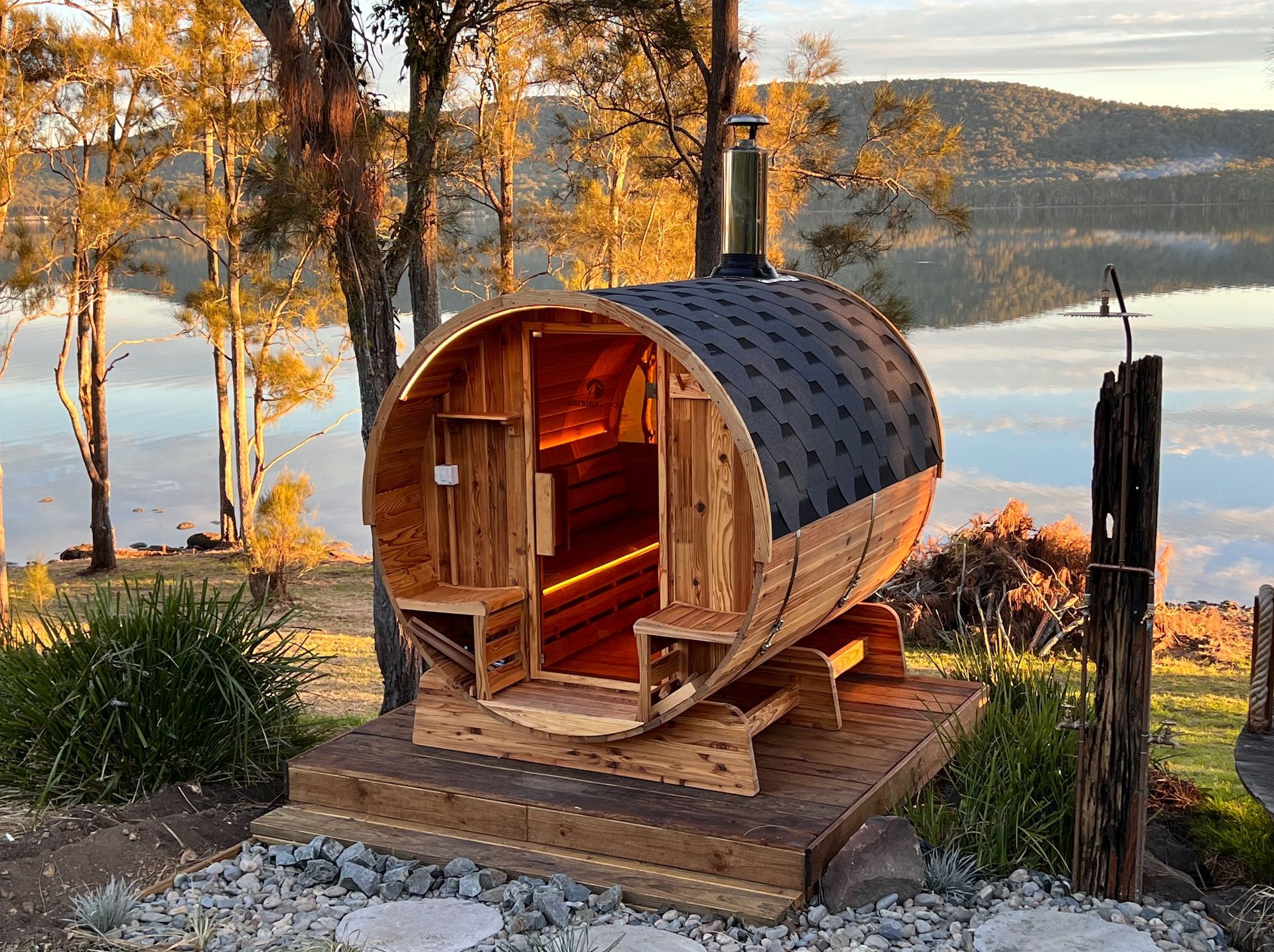 A wooden barrel sauna is sitting next to a lake.