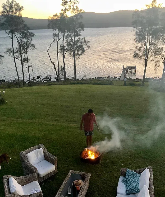A man is standing next to a fire pit with smoke coming out of it.