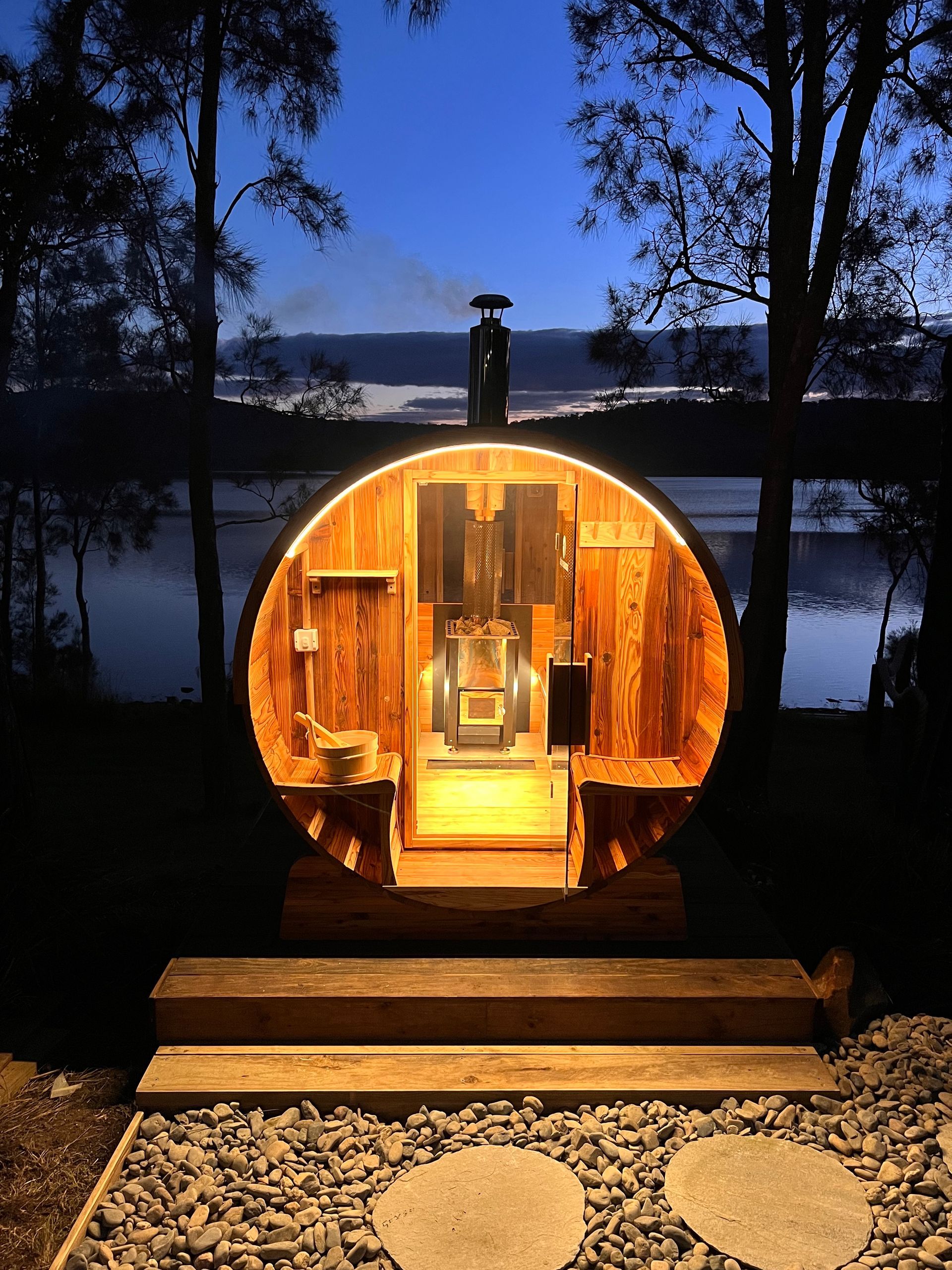A wooden sauna is lit up at night with a view of a lake.