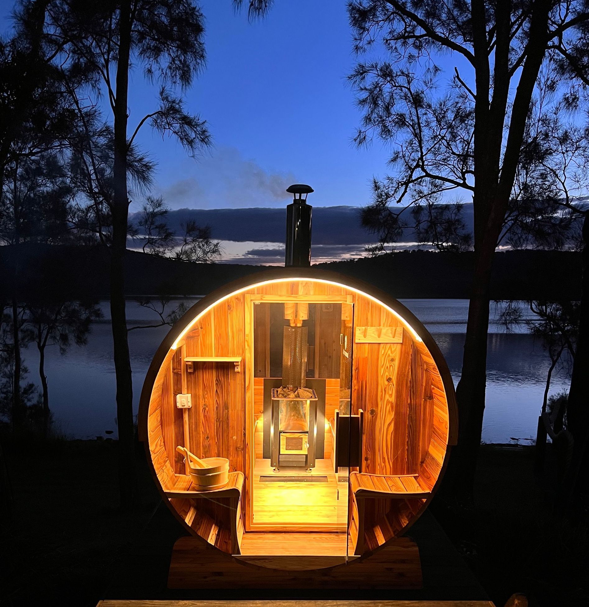 A wooden barrel is lit up at night in front of a lake