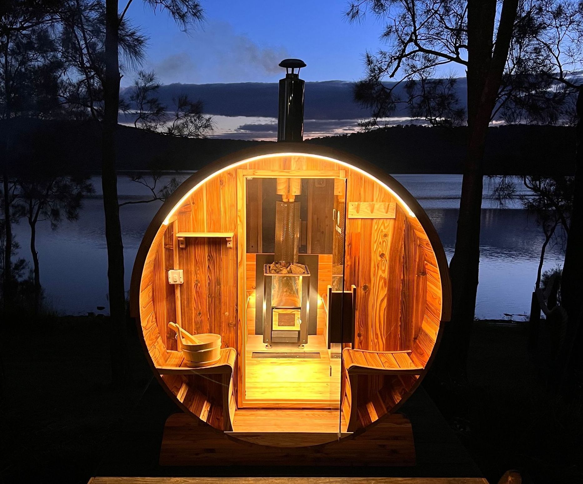 A wooden sauna is lit up at night with a view of a lake.